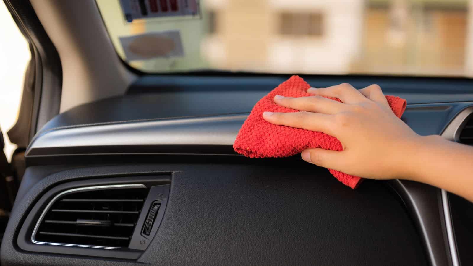 A hand cleaning a car dashboard with a red cloth.