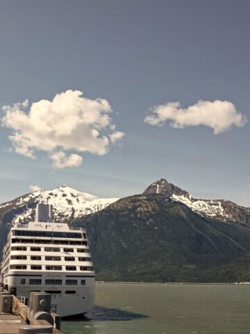 A cruise ship docked at a pier with snow-capped mountains and blue sky in the background—discover your Perfect Cruise for adults and families amidst breathtaking scenery.
