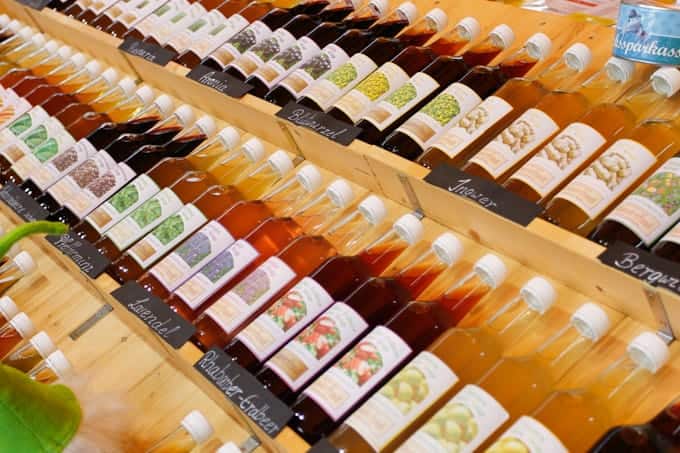 Bottles of fruit syrup arranged on wooden shelves, labeled with various fruit flavors in German.