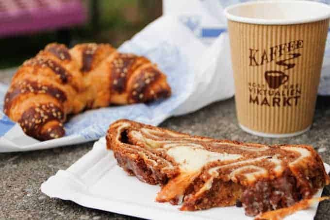 A cup of coffee, a croissant, and a slice of marble cake on a table outdoors.