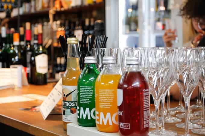 Bottled drinks and wine glasses arranged on a bar counter, with bottles and a person blurred in the background.