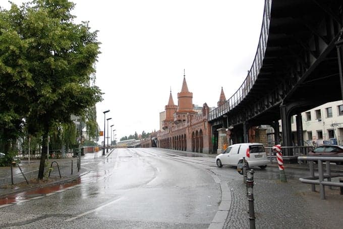 Wet street with a red brick bridge and towers, an elevated railway, and a car on a rainy day.