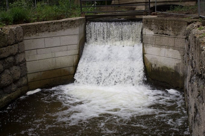 Water flowing over a small concrete dam, creating a waterfall into a pool below.
