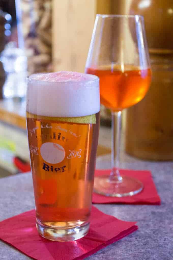 A glass of beer and a glass of orange cocktail on red napkins on a bar counter.