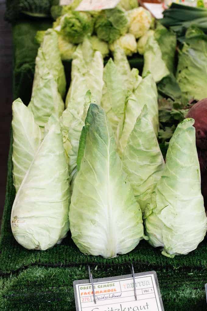 Pointed cabbage heads displayed in a row at a market stall with price tags in front.