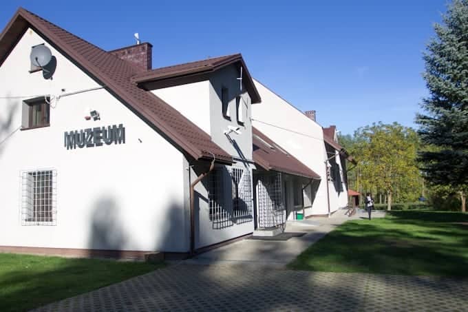 White building with "Muzeum" sign, brown roof, trees, and clear blue sky in the background—a classic scene you might encounter when visiting Poland.