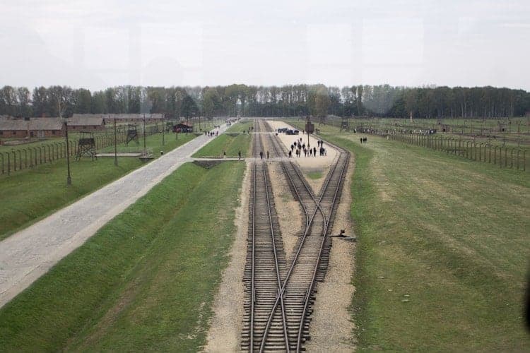 Railway tracks leading into Auschwitz concentration camp, with people walking in the distance on a cloudy day—a somber reminder when visiting Poland.
