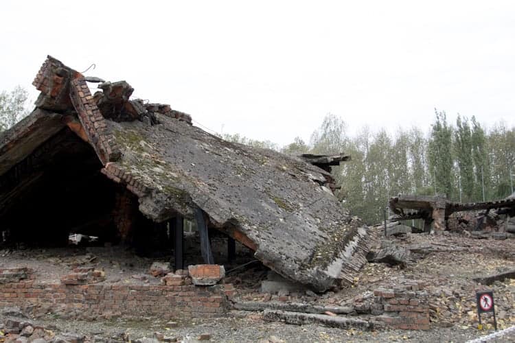 Collapsed brick building with debris scattered around, surrounded by trees under a cloudy sky—a haunting scene you might encounter when visiting Poland.