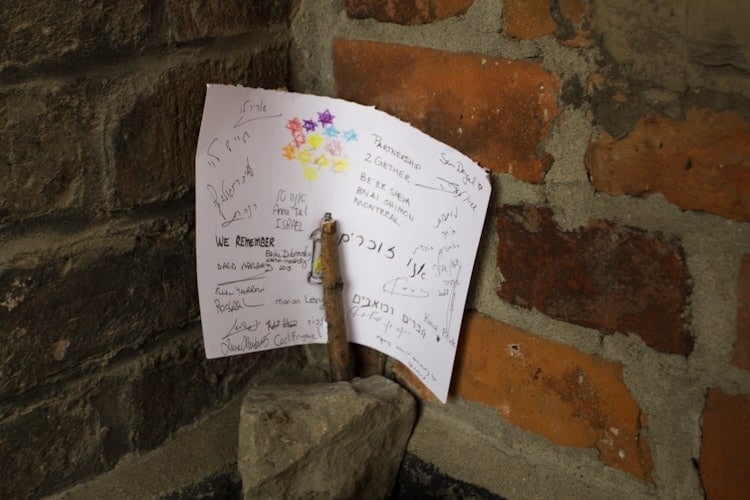 A handwritten note with messages and drawings rests against a brick wall, held by rocks—a small tribute perhaps left by someone visiting Poland.