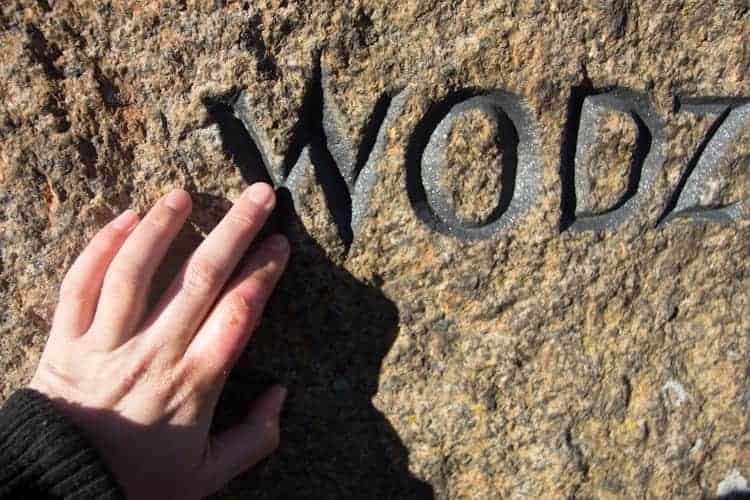 A hand touches rough stone engraved with the word "WODZ" in black letters, capturing a moment of discovery while visiting Poland.