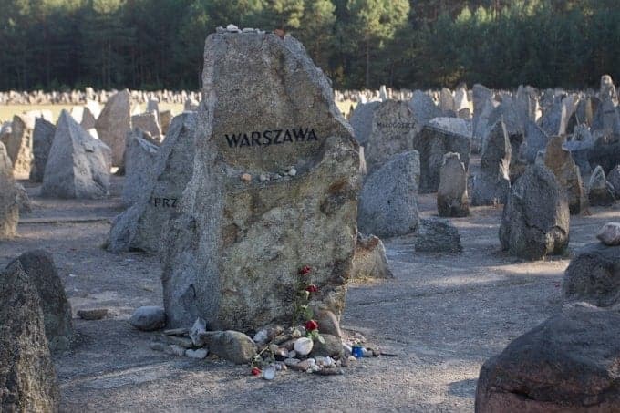 Large stone at a memorial site with "WARSZAWA" inscribed, surrounded by smaller stones and trees—a poignant spot for those visiting Poland.