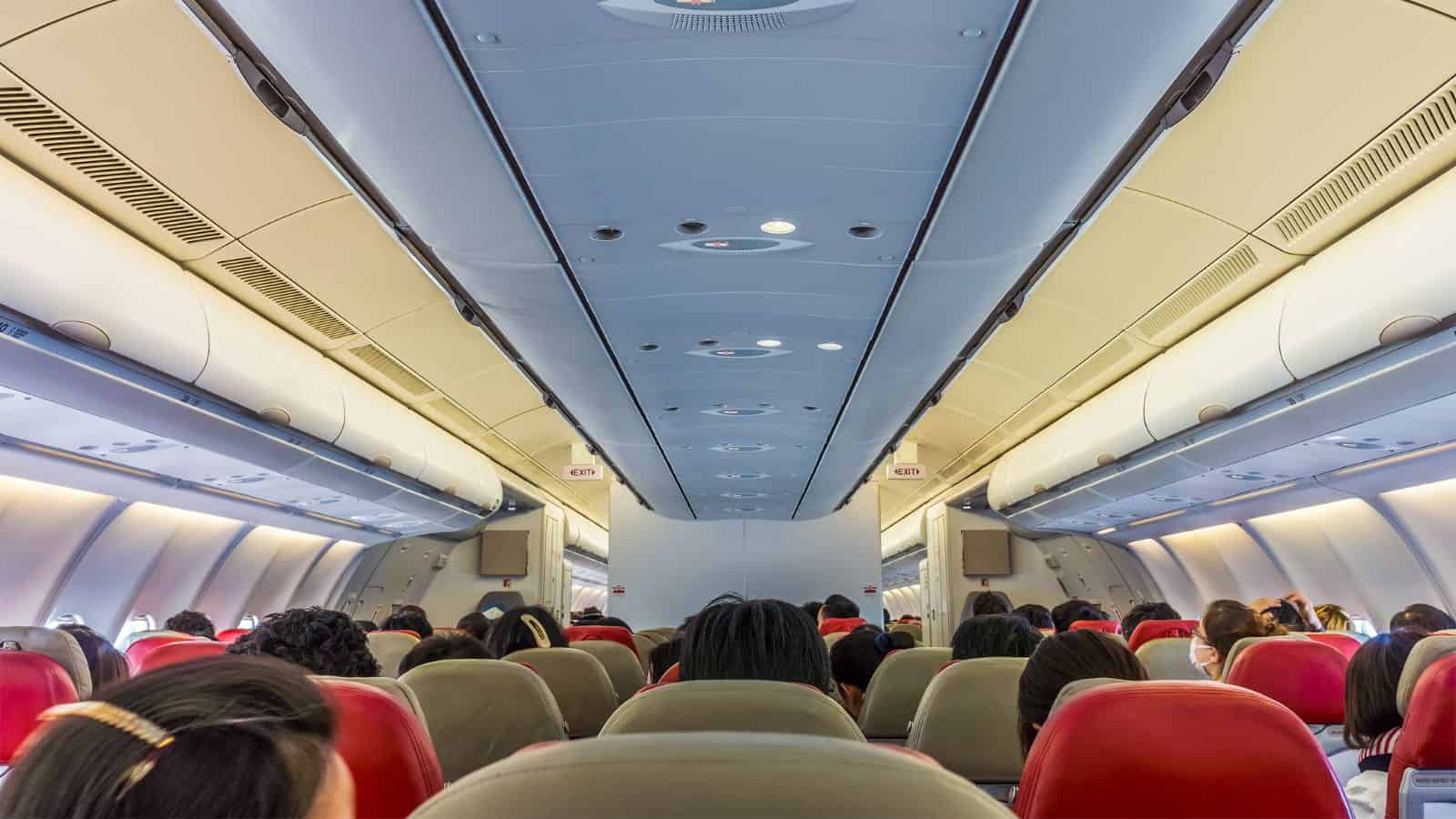 Passengers seated inside an airplane cabin with red headrests and overhead storage compartments evoke old-school travel and cherished travel memories.