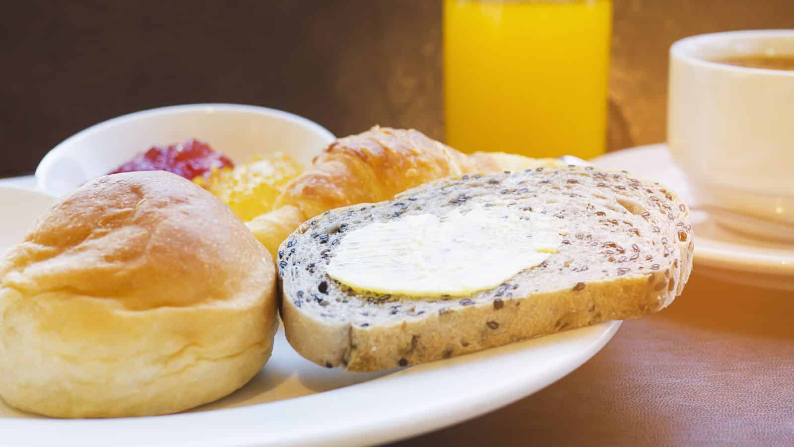 A breakfast plate with bread, croissant, jam, butter, a glass of orange juice, and a cup of coffee.