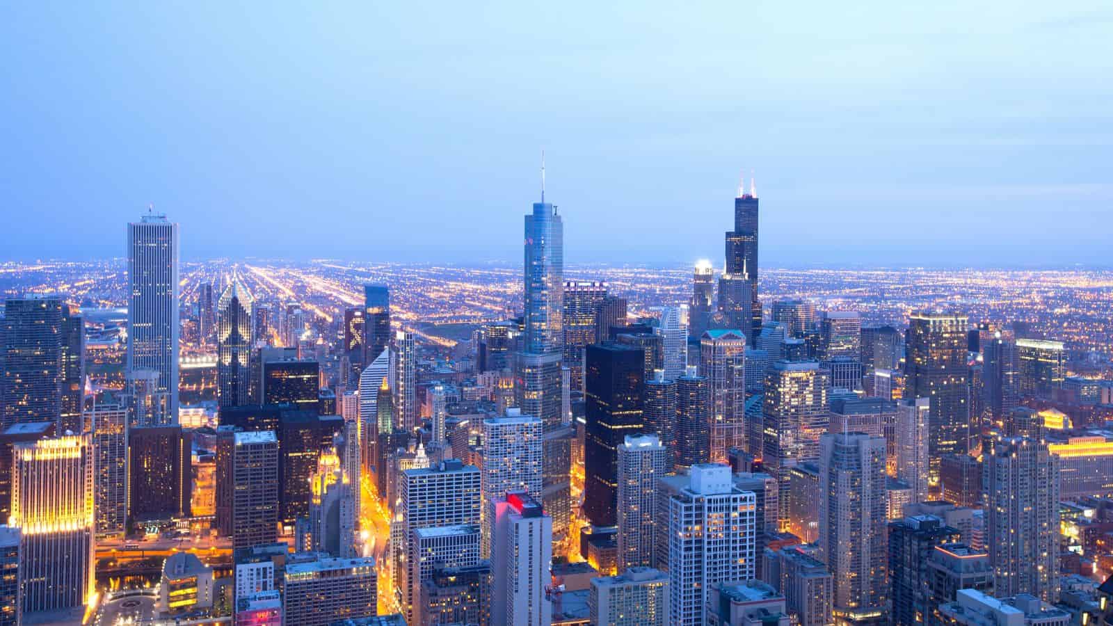 Aerial view of a city skyline at dusk with tall buildings and bright city lights.