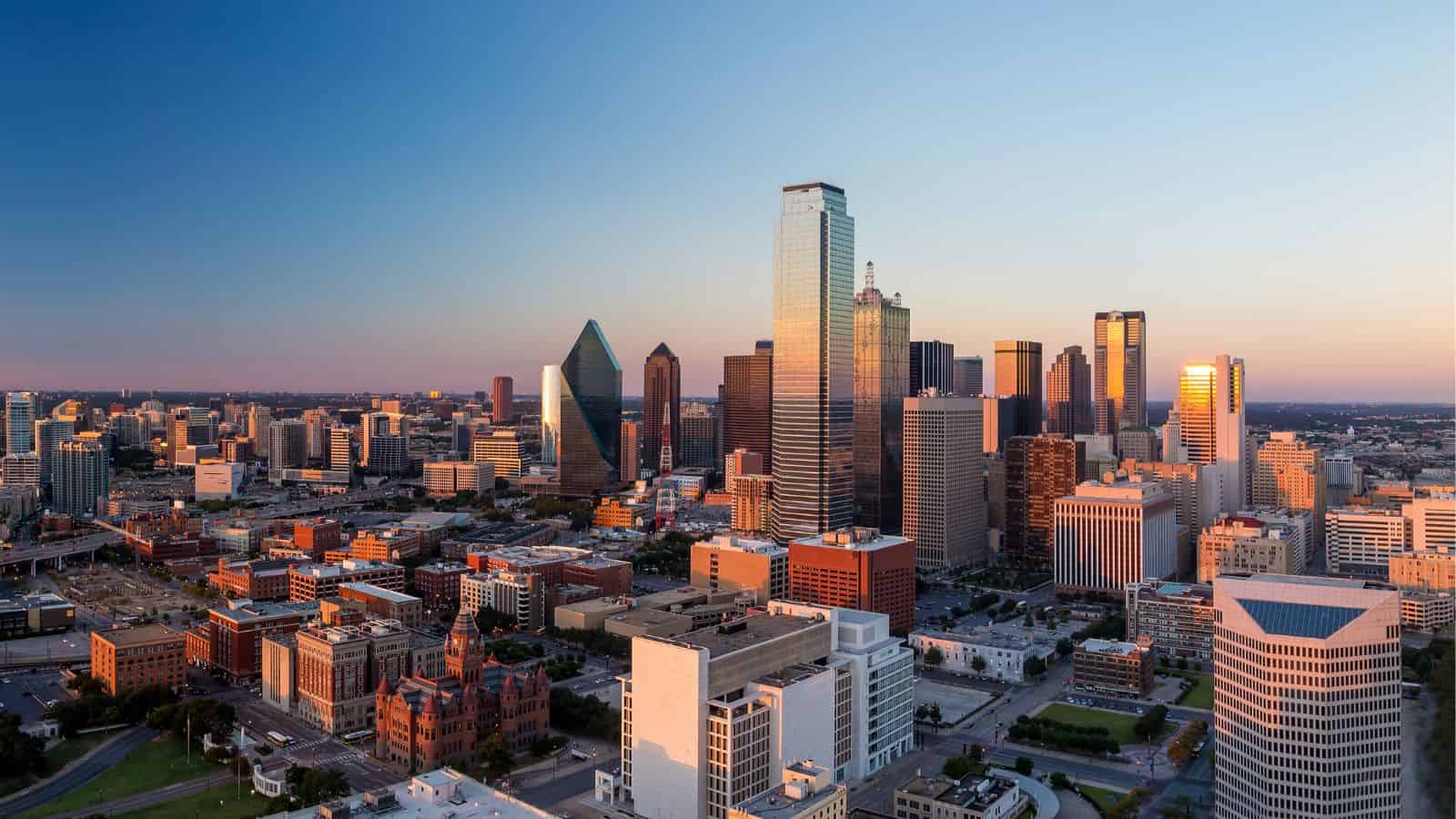 Dallas city skyline at sunset with tall modern buildings and a clear sky in the background.