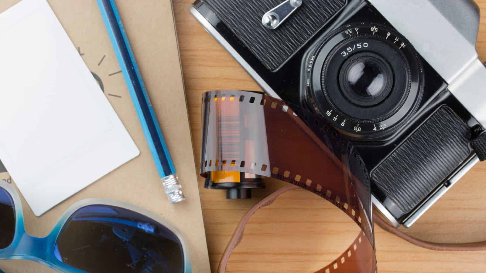 Flat lay of a vintage camera, film roll, instant photo, pencil, sunglasses, and notebook on a wooden surface—capturing the spirit of old-school travel and timeless travel nostalgia.