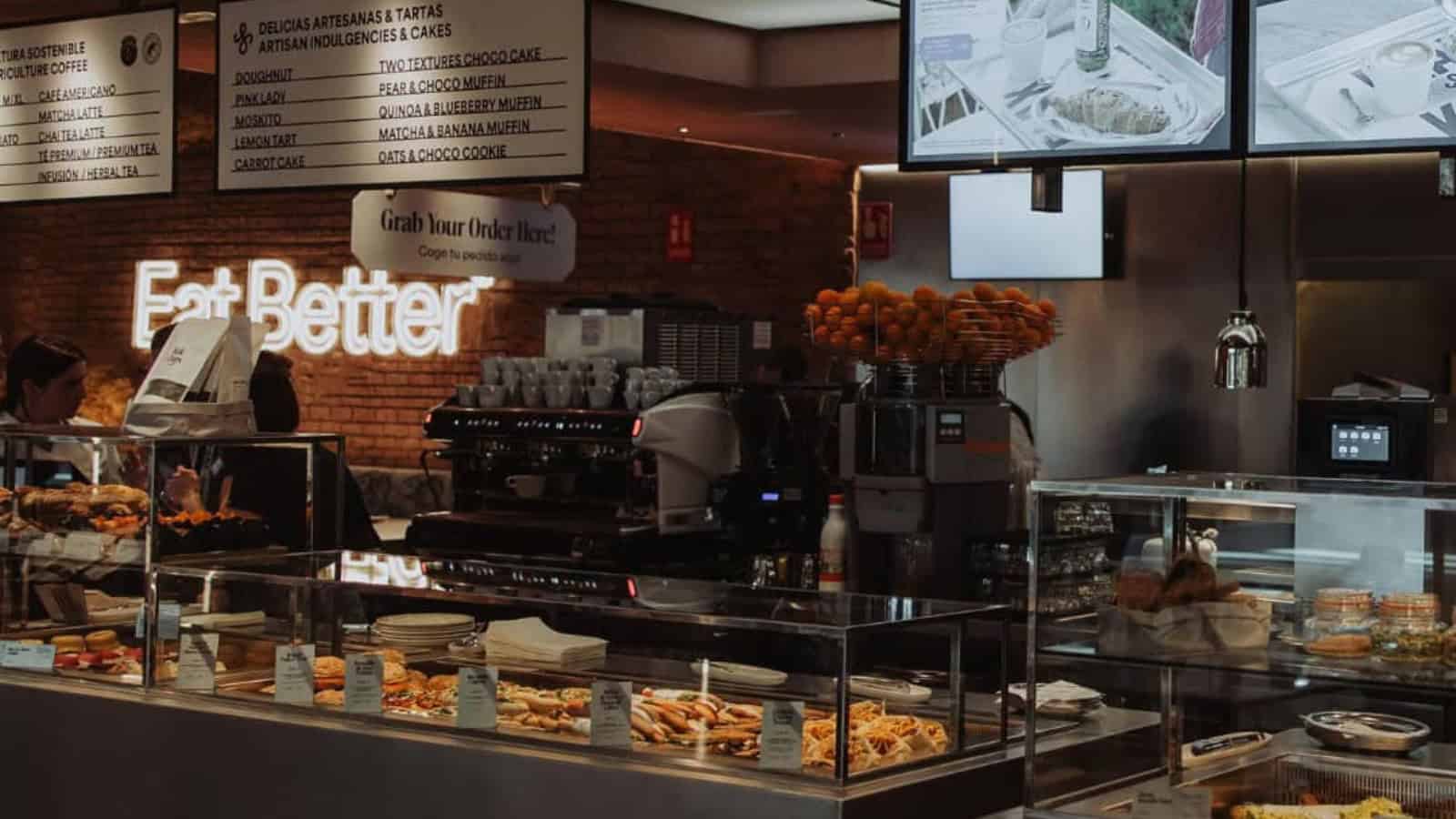 A modern café counter with pastries, coffee machines, and menu boards on the wall—perfect for discovering Gluten Free Barcelona delights.