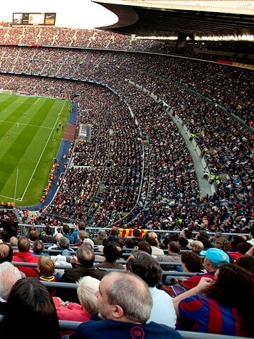 A large, crowded soccer stadium with fans watching a match on a green field.