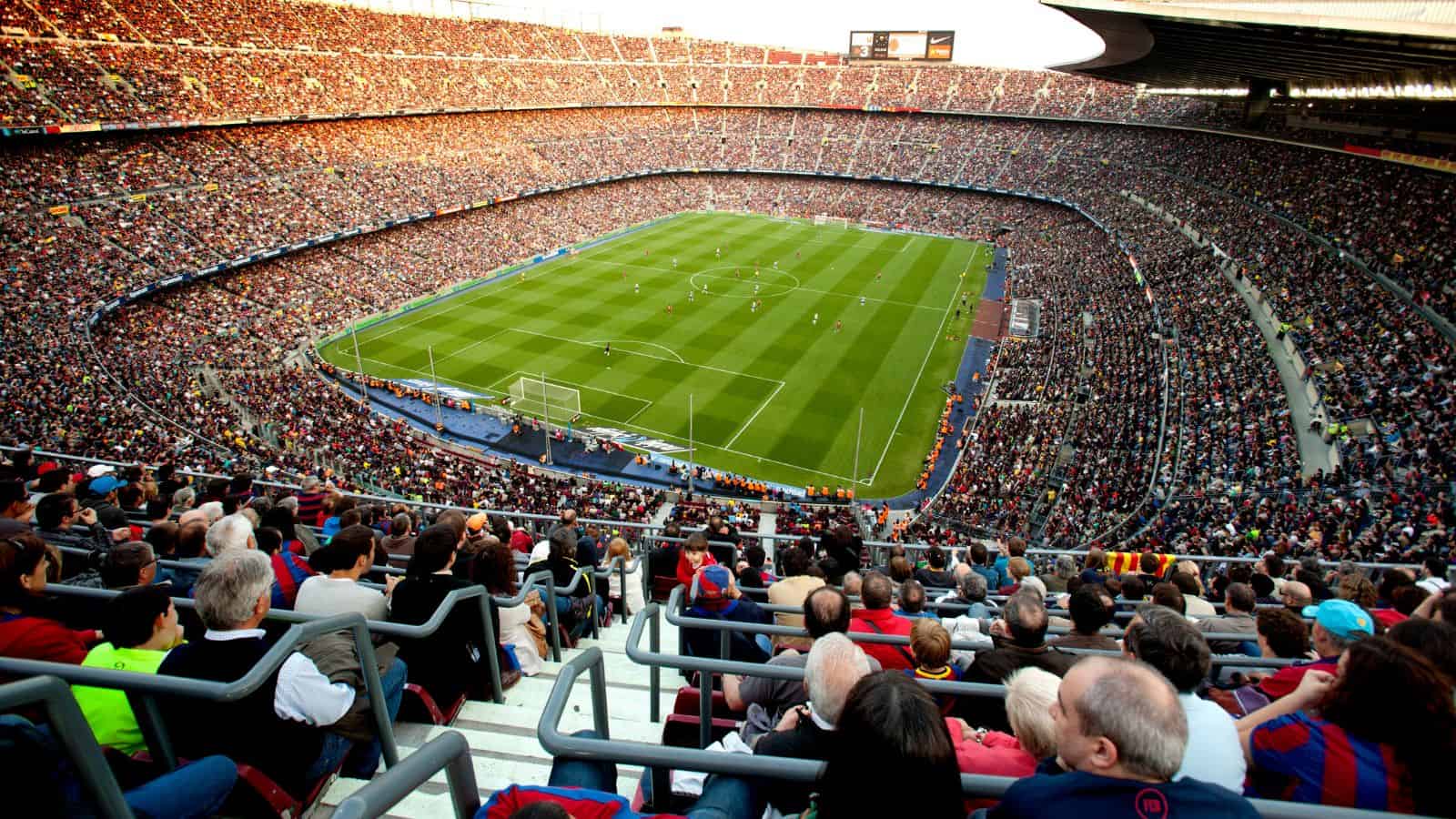 A large, crowded soccer stadium with fans watching a match on a green field.