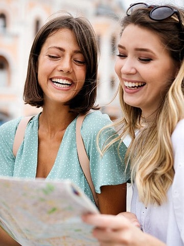 Two young women smiling and looking at a map outdoors in a city setting.