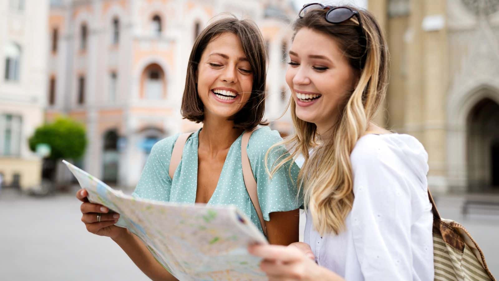 Two young women smiling and looking at a map outdoors in a city setting.