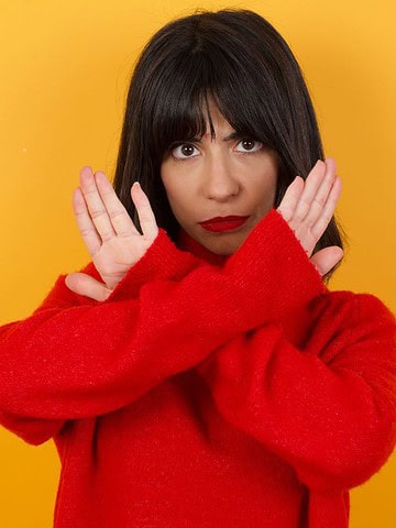 Woman in a red sweater crossing her arms in front of her chest against a yellow background, expressing concern—perhaps thinking about travel safety in December or which countries to avoid during the holiday season.