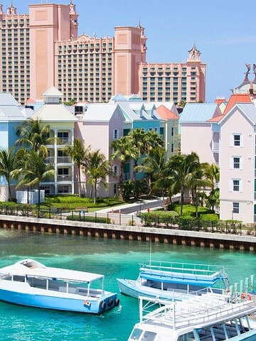 Colorful waterfront buildings and boats with a large pink resort in the background under a clear blue sky.