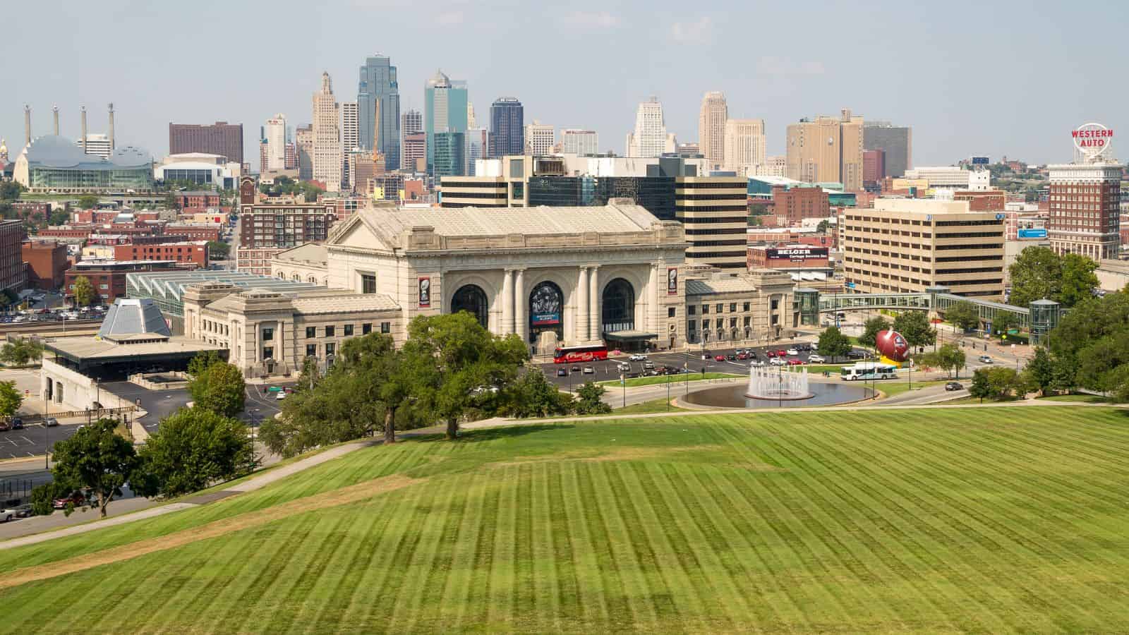 Kansas City skyline with Union Station in foreground and green lawn in the front on a clear day.