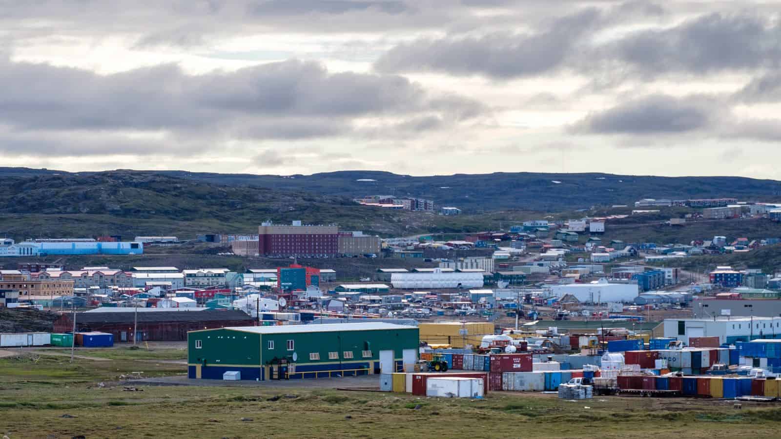 Town with colorful buildings and shipping containers on a grassy landscape under a cloudy sky.