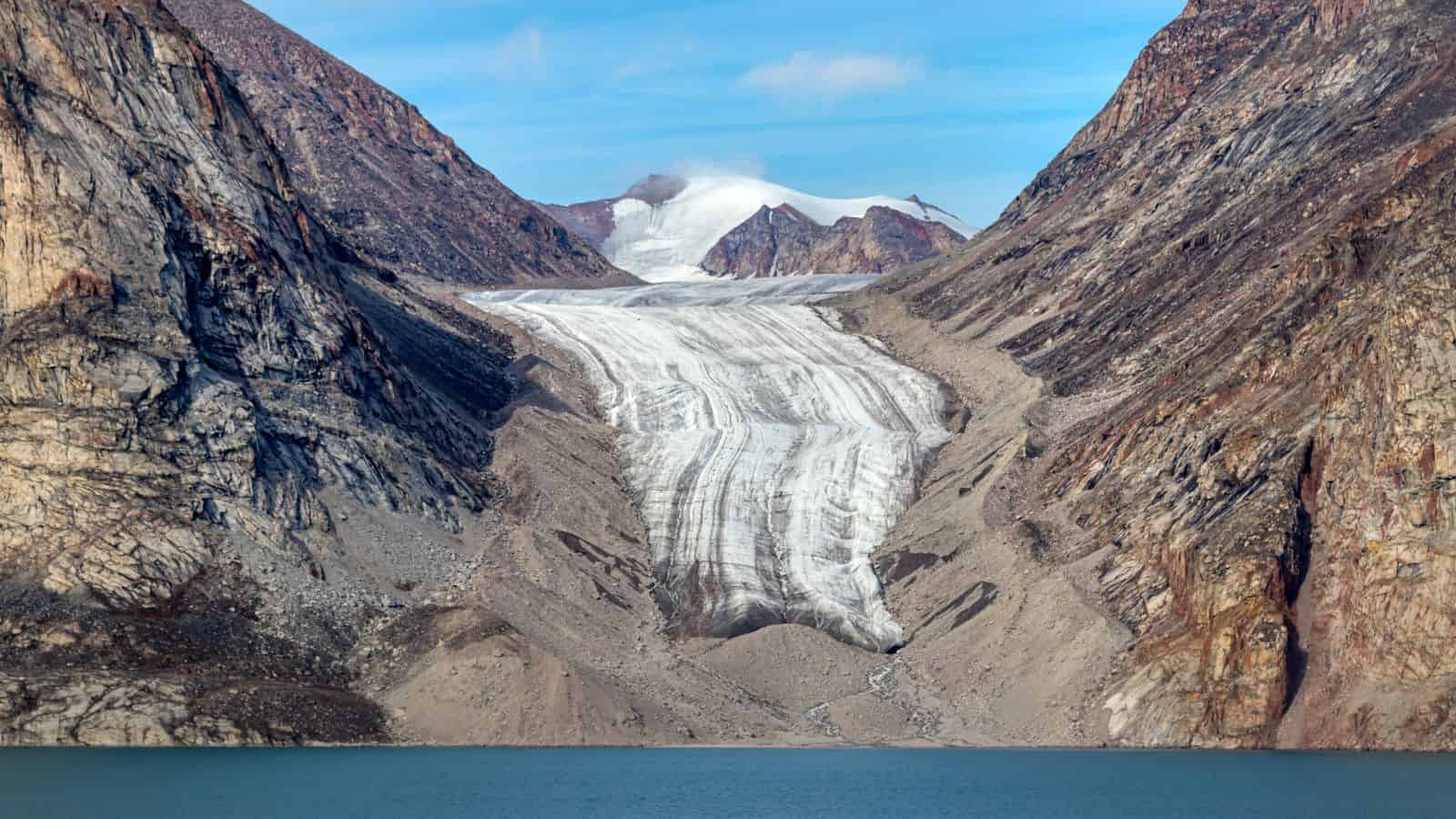 A glacier flows between rocky mountains, ending near a blue lake under a clear sky.