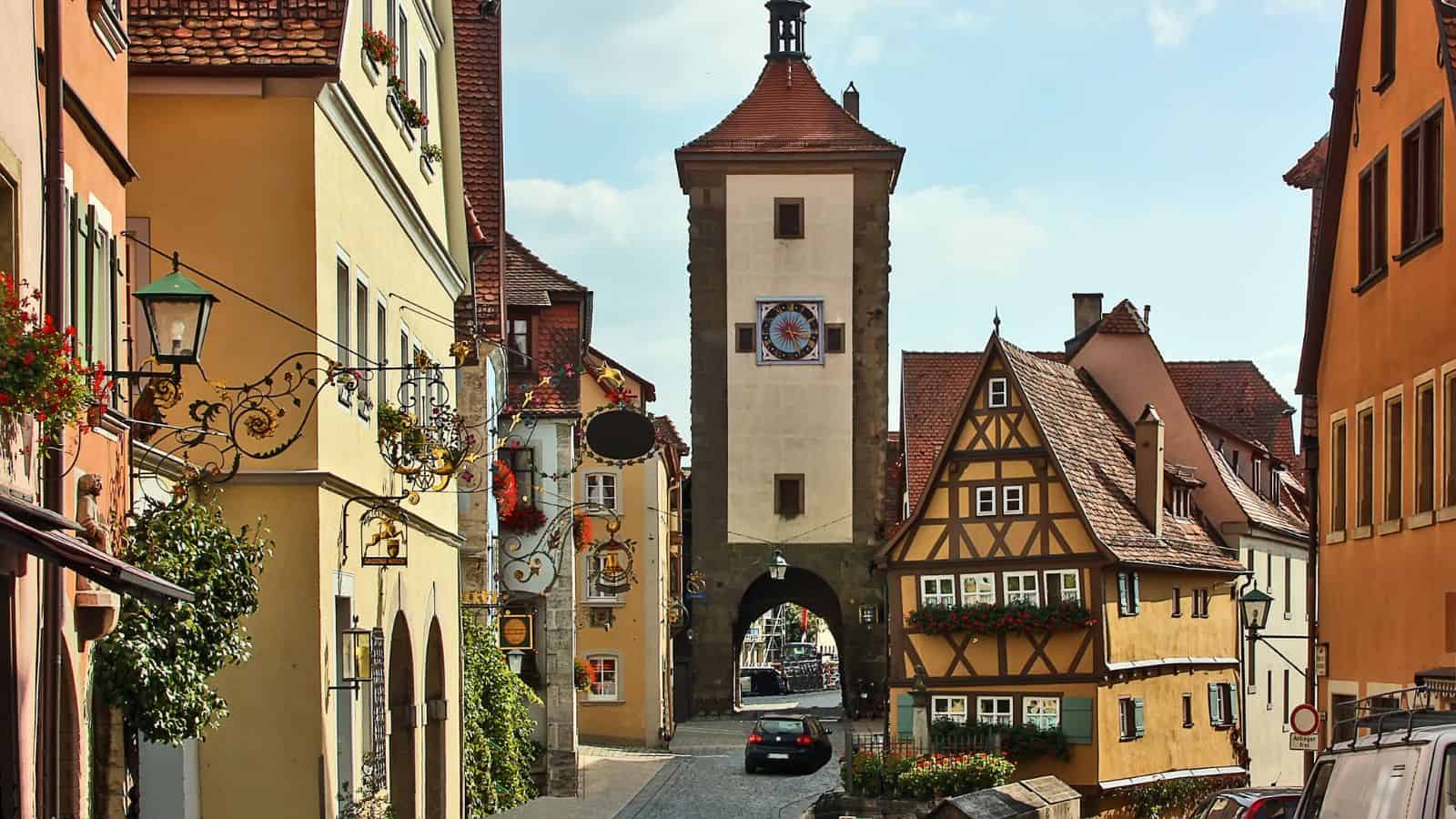A cobblestone street with colorful historic buildings and a medieval tower in a European town.