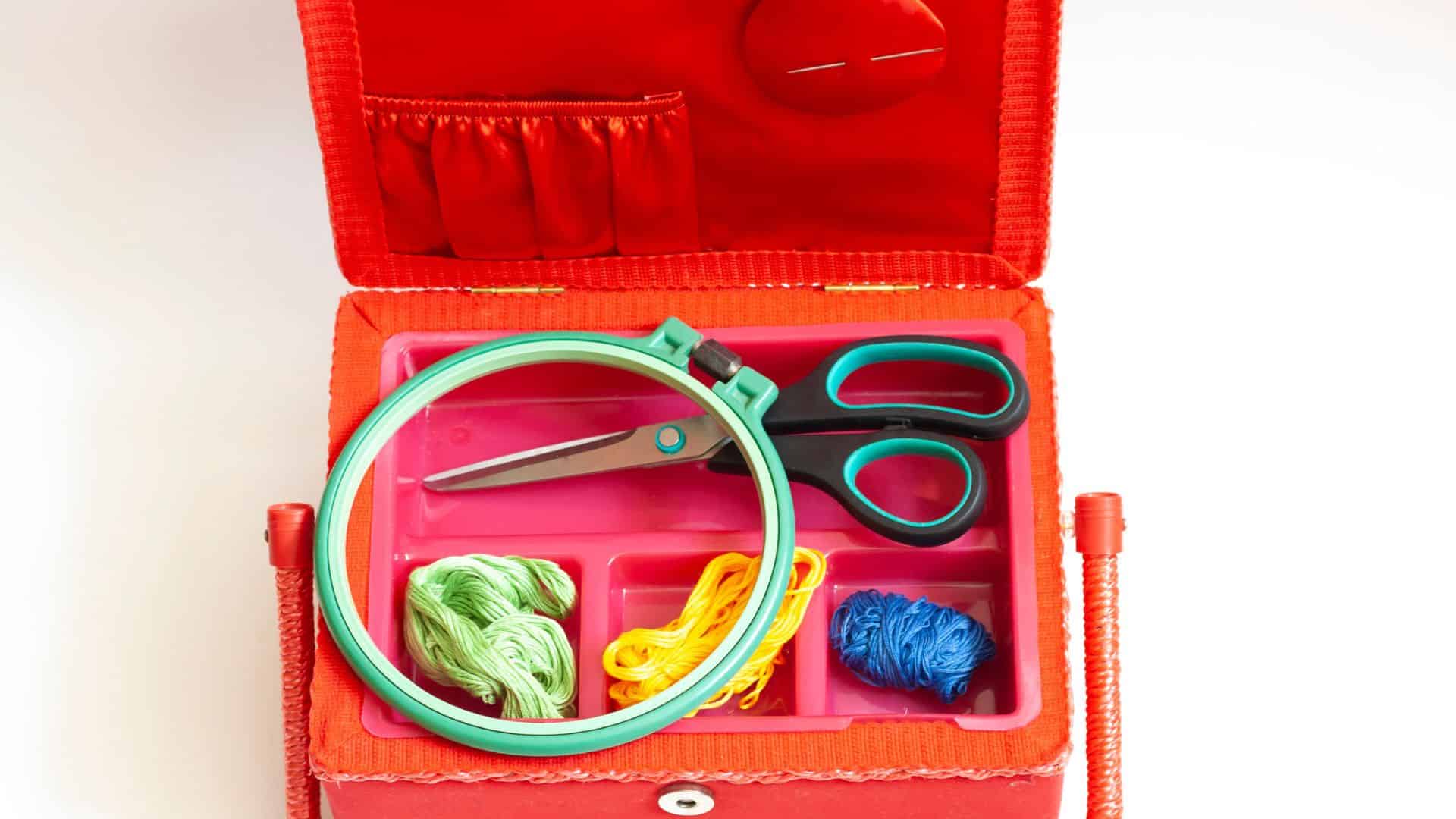 Open sewing box with scissors, embroidery hoop, and colorful threads arranged in compartments.