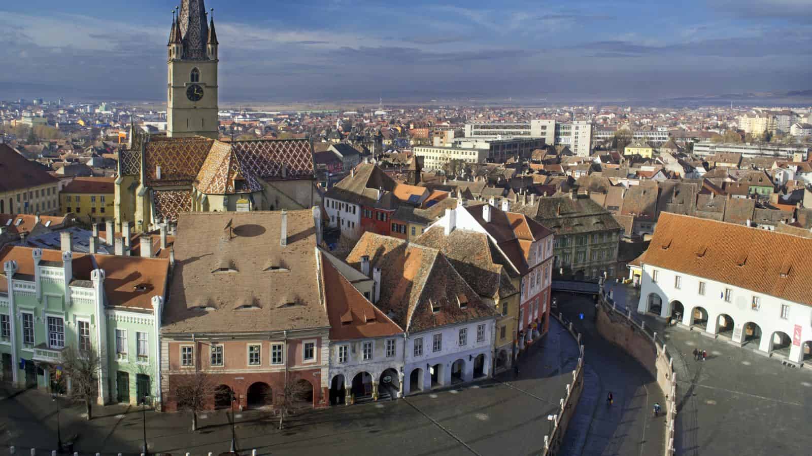 Aerial view of a historic European town square with colorful buildings and a tall clock tower.