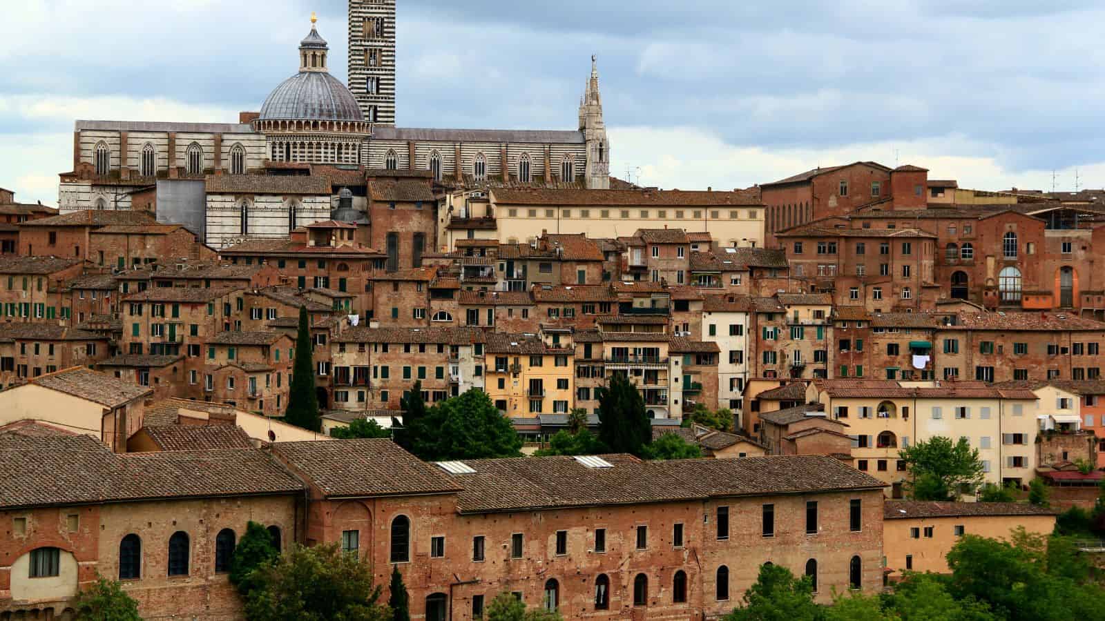 View of Siena, Italy with terracotta rooftops and the cathedral's dome and tower in the background.