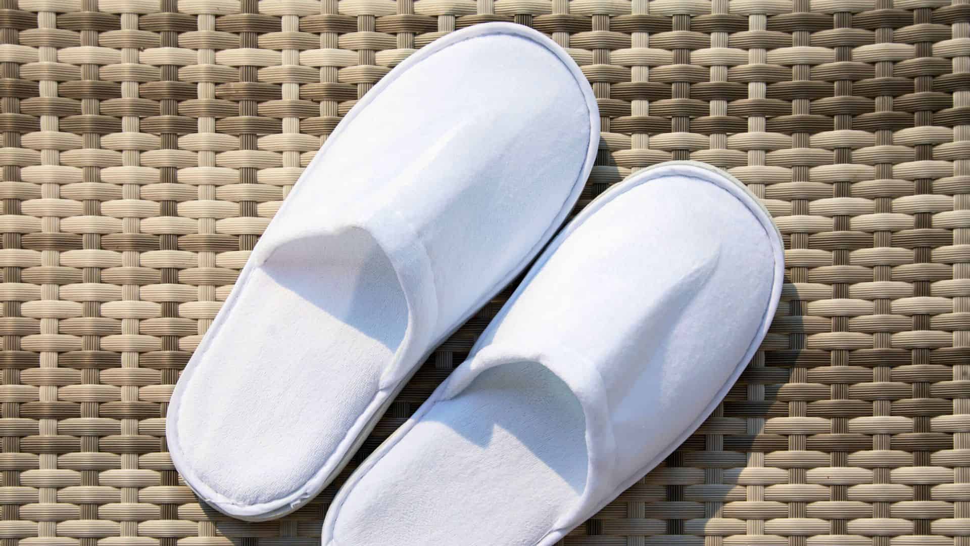 A pair of white slippers placed on a woven beige surface.