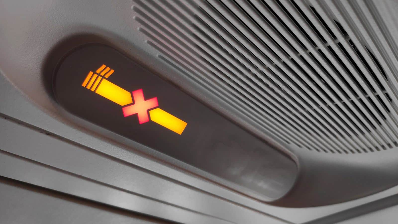Illuminated no smoking sign on an airplane ceiling next to an air vent, evoking travel nostalgia and memories of old-school travel.