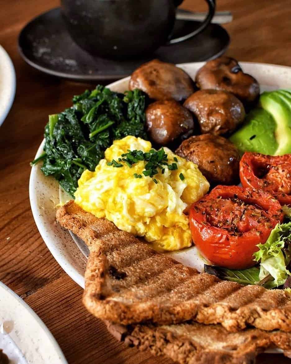 A plate with scrambled eggs, toast, sautéed spinach, grilled mushrooms, tomatoes, and avocado—a perfect Gluten Free Barcelona breakfast option.