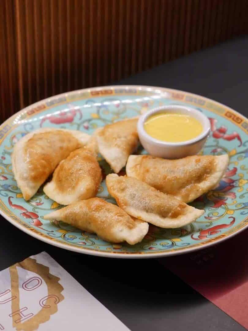 Six pan-fried dumplings on a decorative plate with a small bowl of yellow dipping sauce—perfect for anyone seeking gluten free options in Barcelona.
