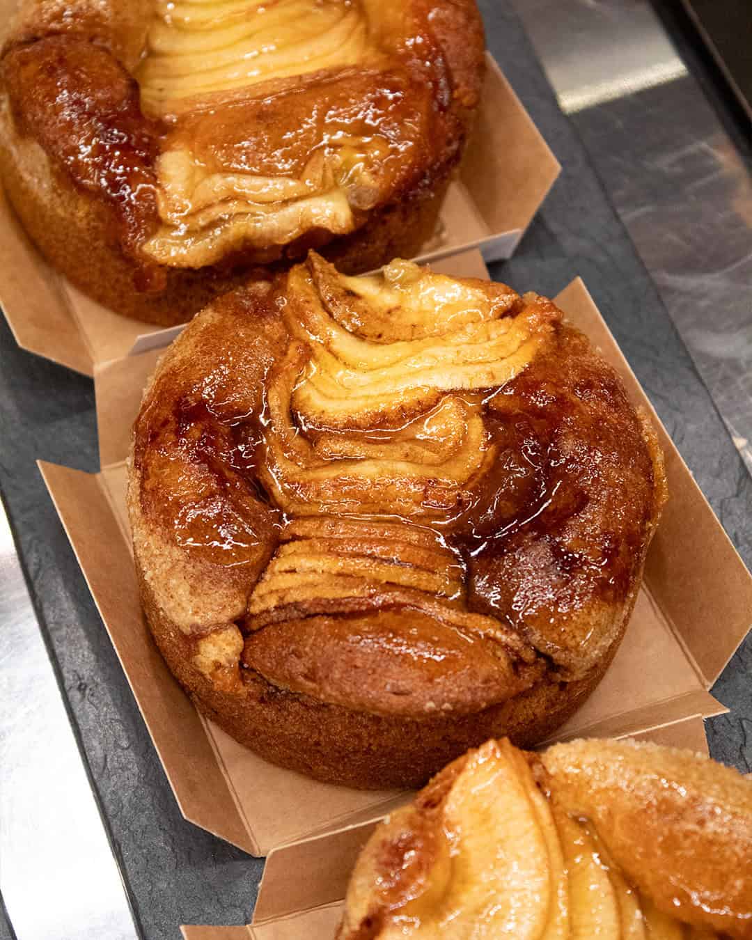 Glazed apple cakes with caramelized apple slices on top, served in small square paper trays—a perfect gluten free treat to enjoy in Barcelona.