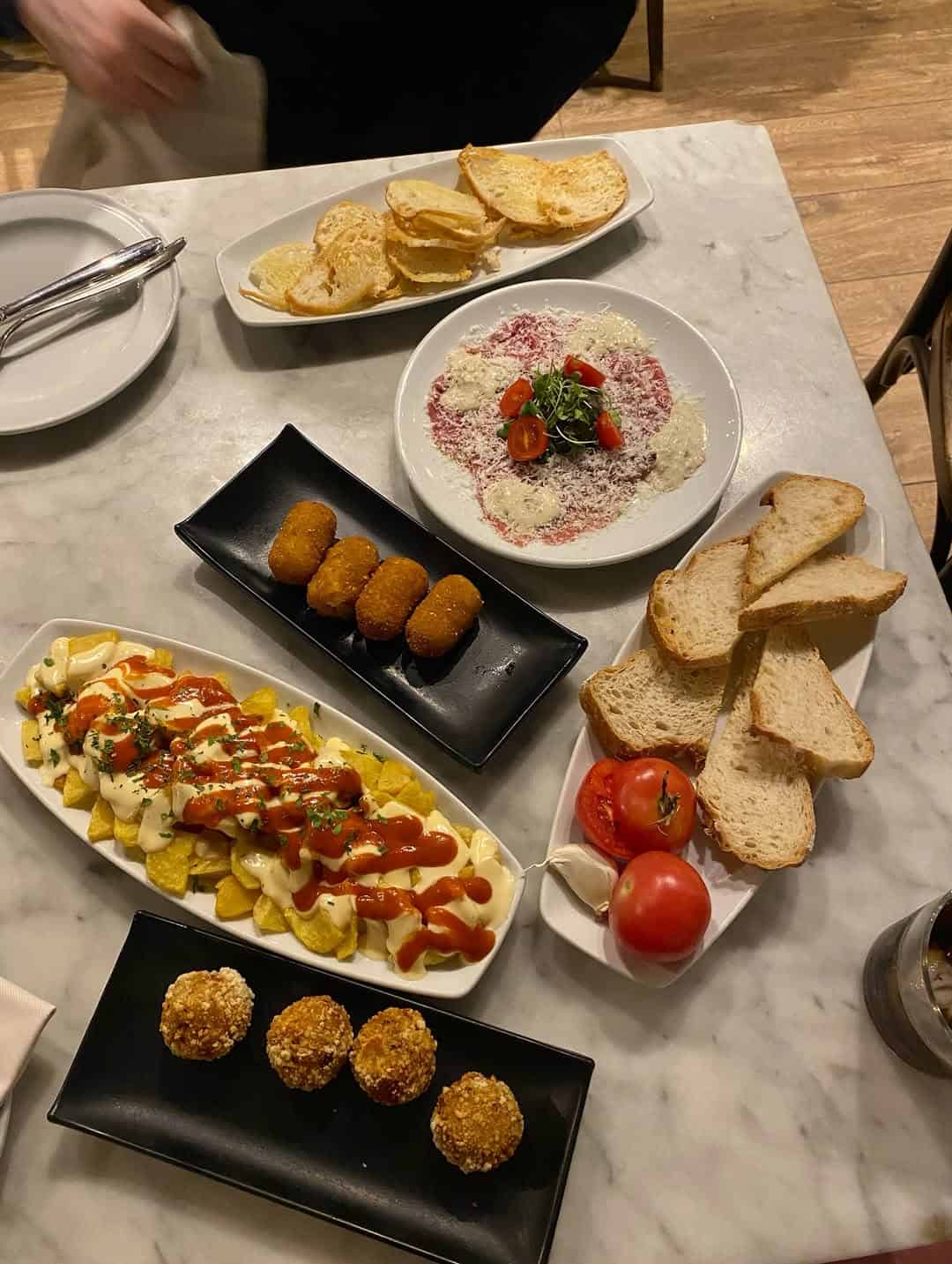 A table with assorted tapas, including bread, croquettes, potatoes with sauce, and sliced tomatoes—perfect for anyone exploring gluten free Barcelona options.