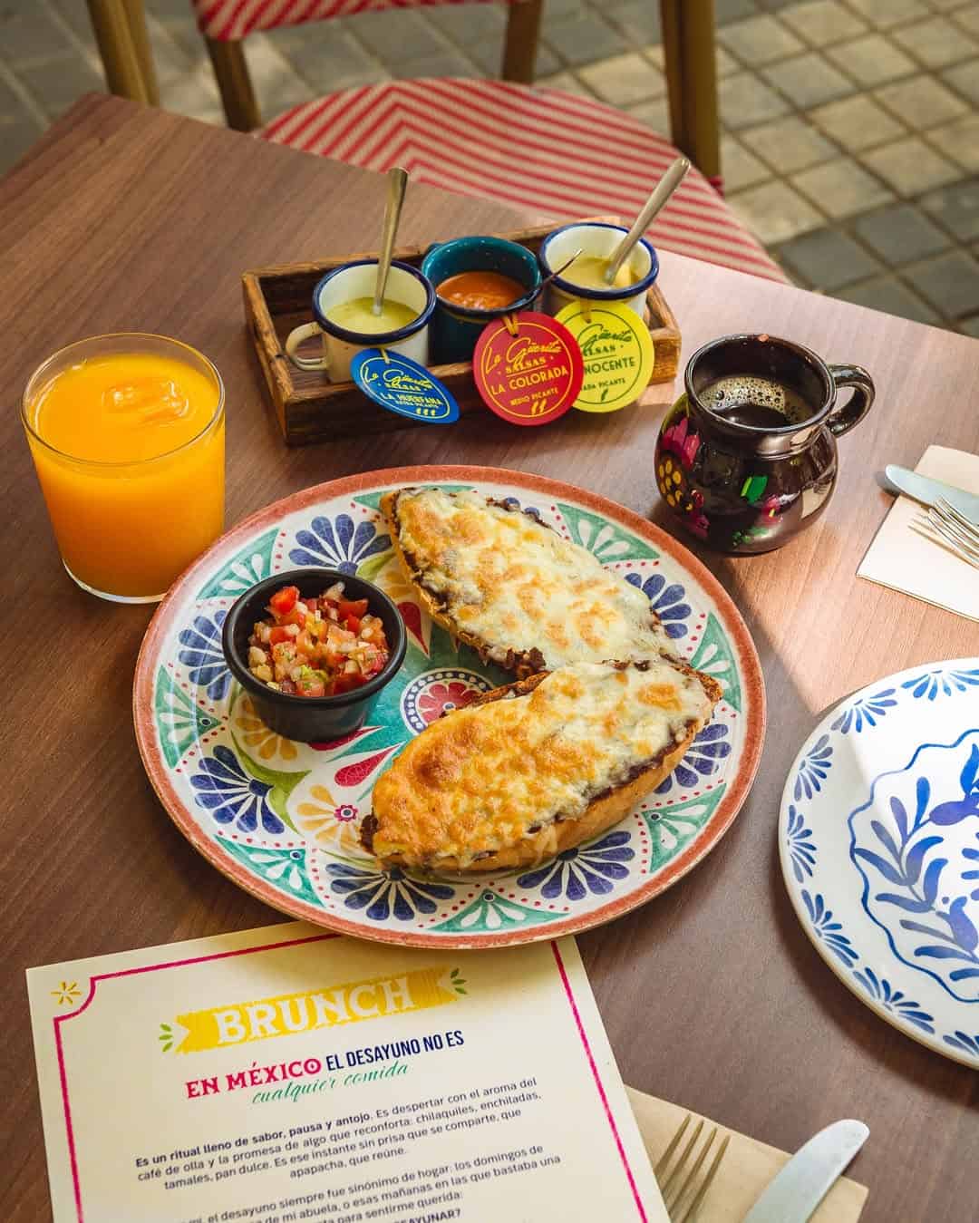 A colorful plate with cheesy bread, salsa, orange juice, sauces, and coffee on a wooden table—a perfect glimpse of Gluten Free Barcelona delights.
