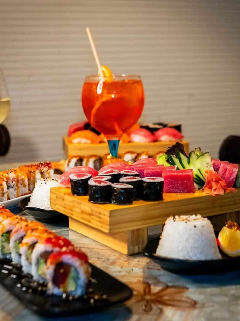Colorful sushi rolls and sashimi on wooden trays, with wine, a cocktail, and rice on a table—perfect for those seeking Gluten Free Barcelona dining options.