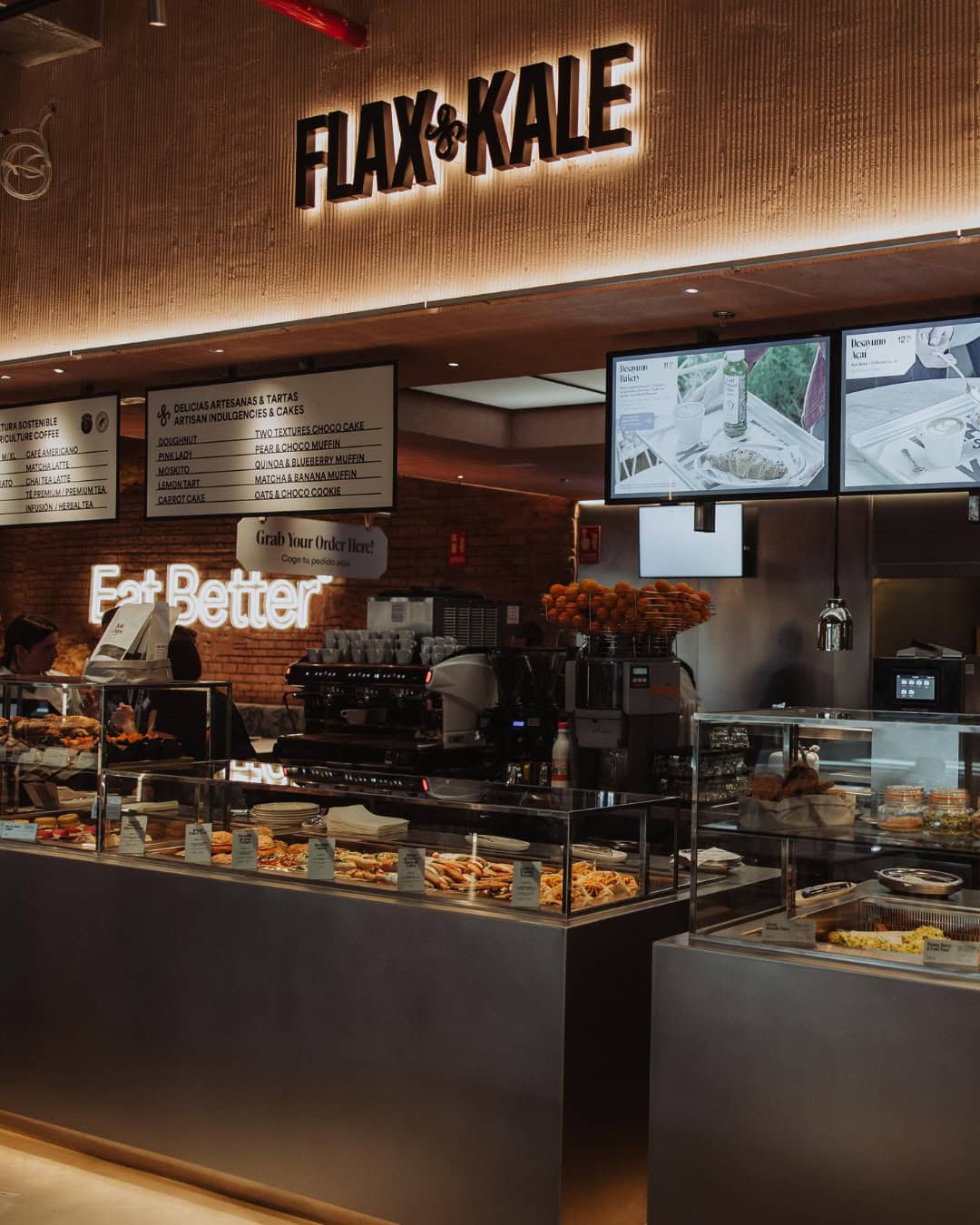 Modern café interior with “FLAX & KALE” sign, pastry display, digital menus, and barista behind the counter—a standout spot for Gluten Free Barcelona treats.