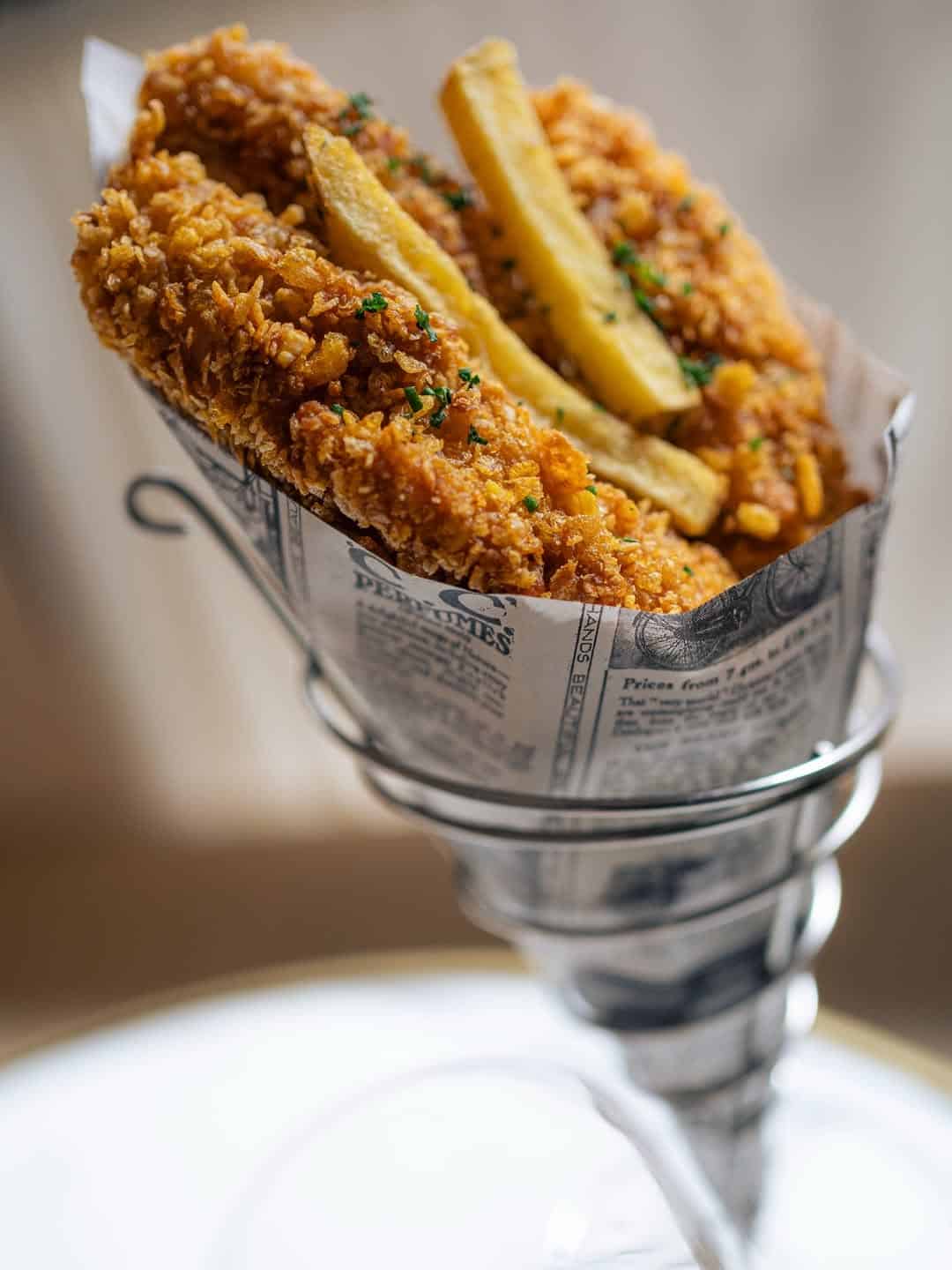 Crispy fried fish and French fries served in a paper cone lined with newspaper print—a delicious taste of Gluten Free Barcelona.