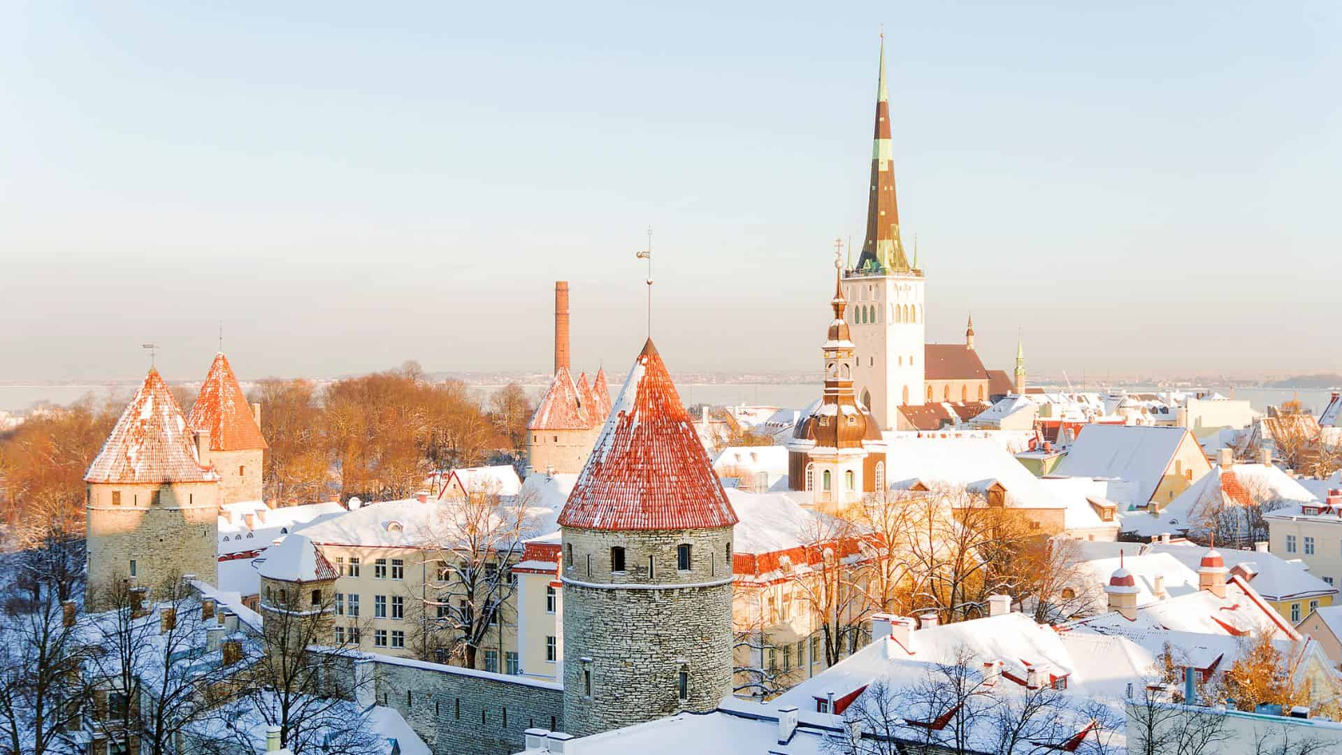 Snow-covered medieval buildings and church spires in Tallinn, Estonia, on a clear winter day.