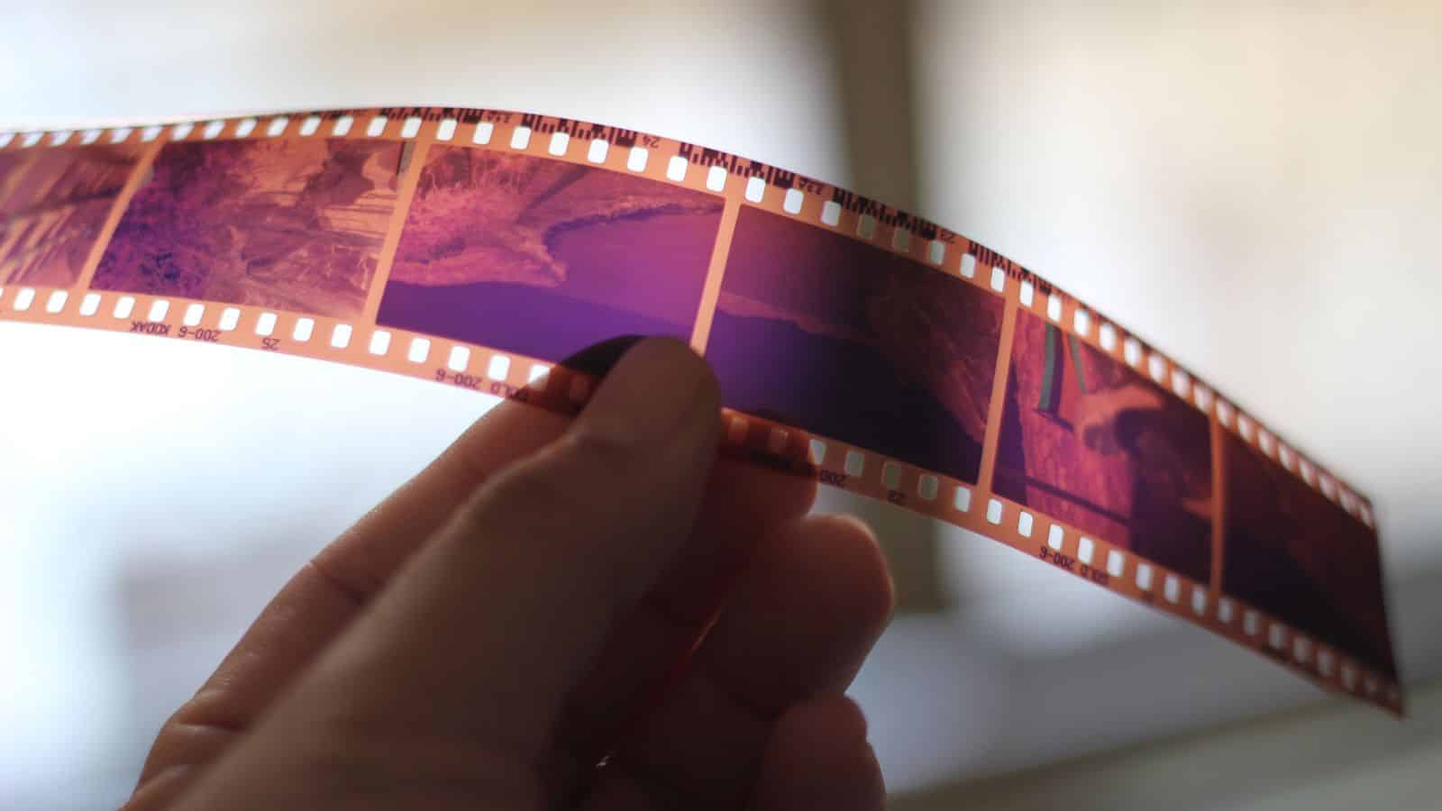 A hand holds a strip of 35mm photographic film negatives up to the light, revealing multiple frames—capturing Old-School Travel memories cherished by Boomers.