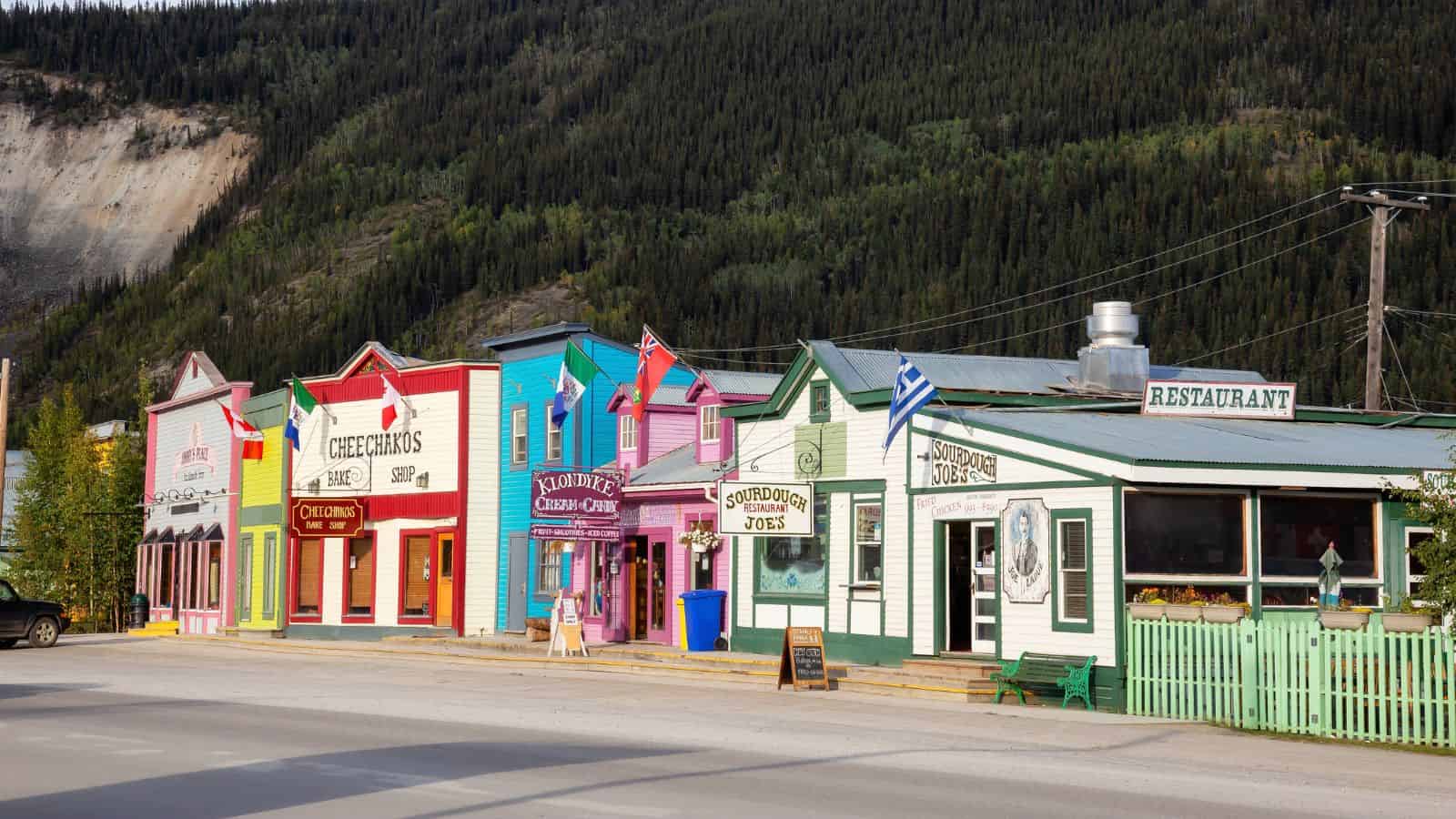 Colorful historic storefronts line a quiet street with forested hills in the background.