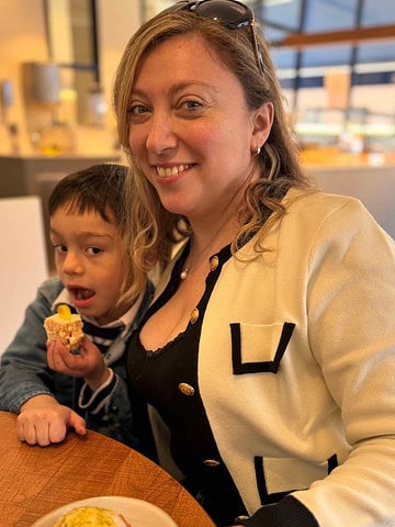 A woman smiles at a table with a young boy eating a snack beside her in a bright, gluten free Barcelona café.