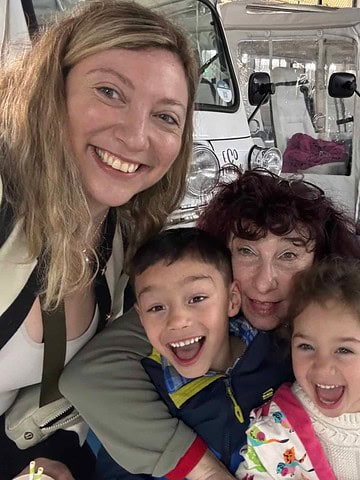 Three smiling people and two laughing children pose for a selfie in front of a white tuk-tuk indoors, capturing joyful moments and discovering tips to make traveling with kids easier in 2025.