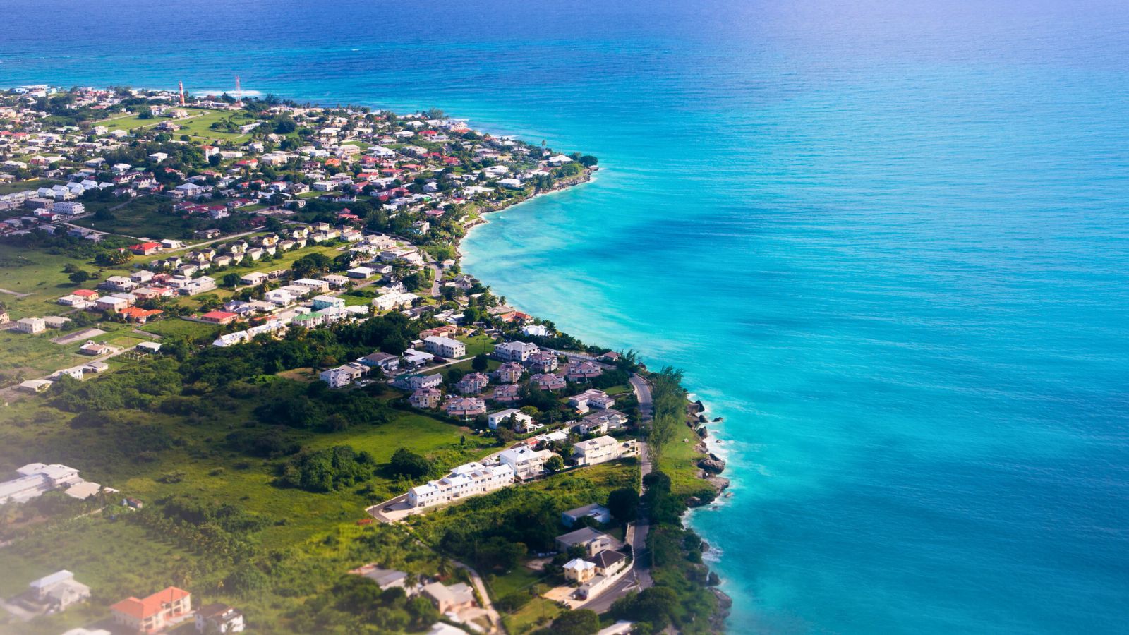 Aerial view of a coastal town with houses near turquoise blue ocean water and lush green landscape.
